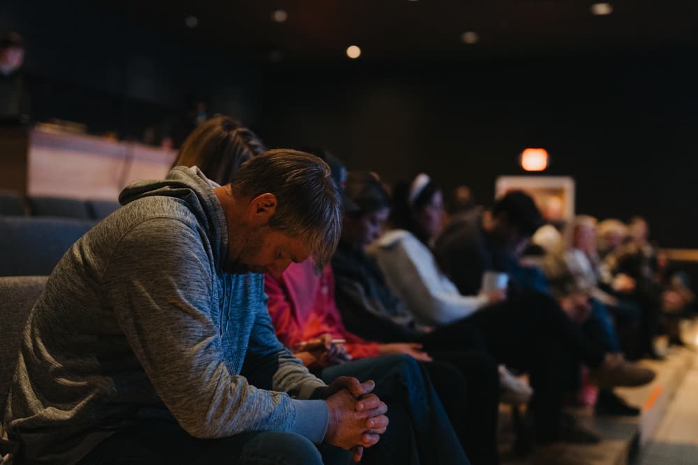 A man seated with his head bowed and hands clasped in prayer during a Brighthouse Church gathering