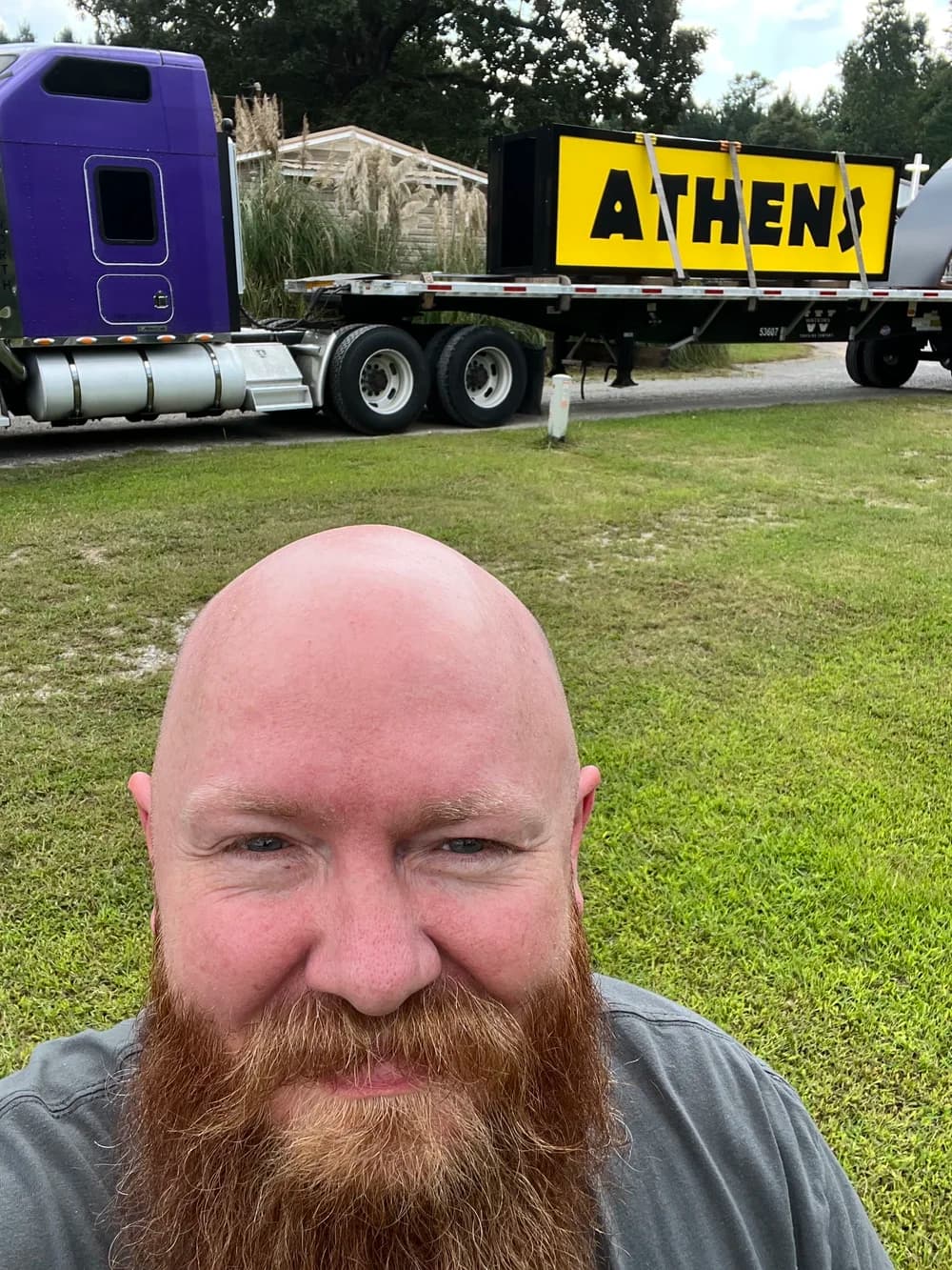 Derek Dale smiling in front of a flatbed truck carrying a large sign reading ATHENS