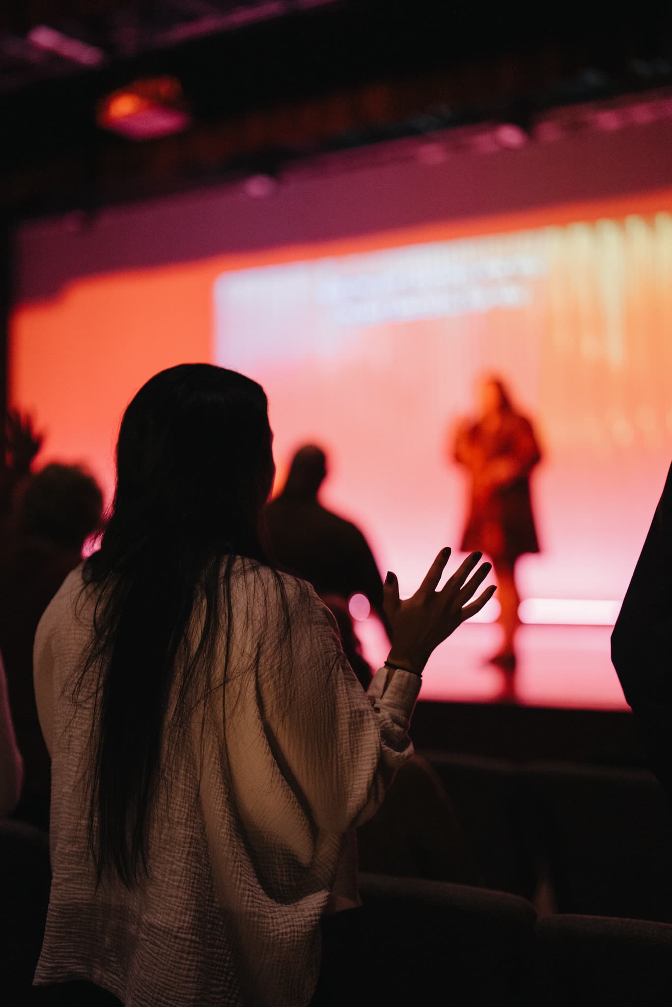 A woman with her hand raised in worship facing the stage