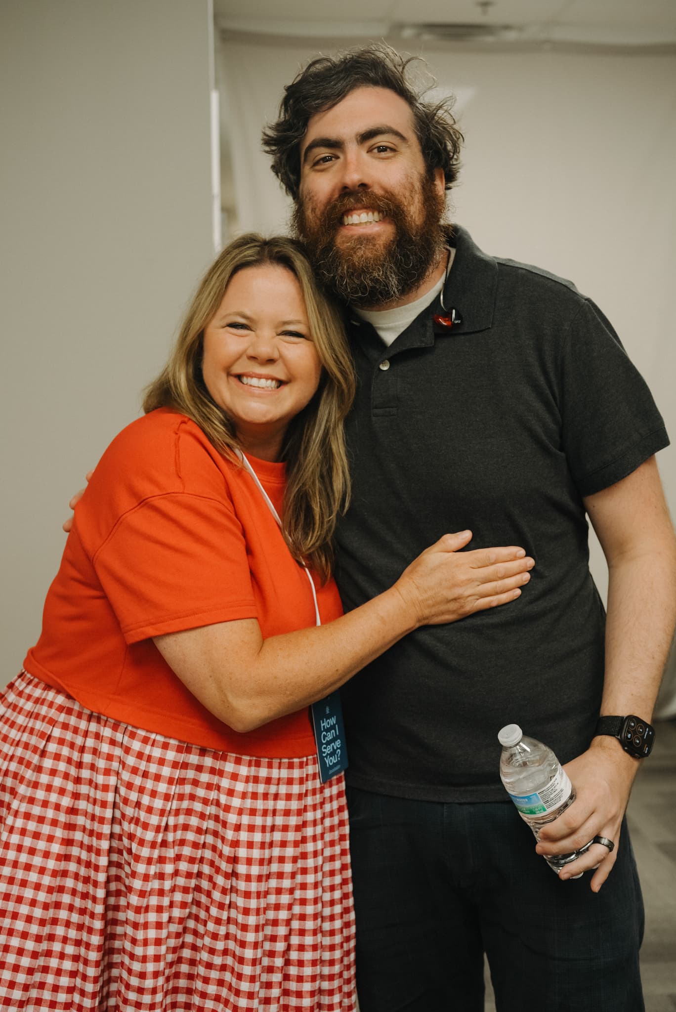 A smiling Brighthouse volunteer wearing a How Can I Serve You lanyard hugging a guest